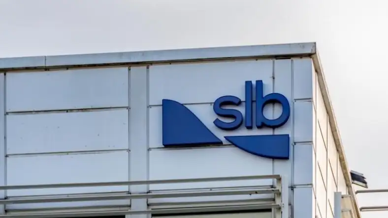 SLB branded building with a blue geometric logo and lettering on a white industrial facade under grey sky