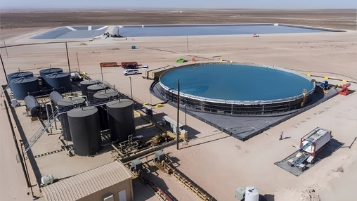Aerial view of a desert water recycling facility with a large circular blue tank and dark storage tanks