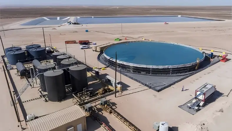 Aerial view of a desert water recycling facility with a large circular blue tank and dark storage tanks